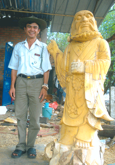 Đạo hữu Tịnh Tín đứng bên sản phẩm điêu khắc gỗ - tượng Đạt Ma Tổ Sư