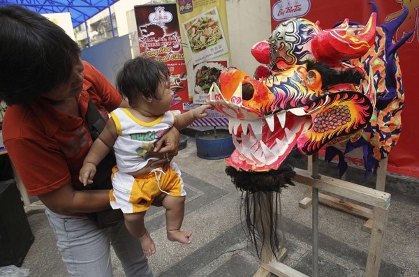 Bà mẹ đang bế cậu con trai trước một đầu chú rồng múa rối ở một gian hàng người Trung Quốc tại thủ đô Manila, Philippines. Ảnh: Chinadaily
